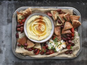 Herkullinen napostelutarjotin jossa hummus-dippi, leivänpaloja, oliiveja, fetaa ja tomaatteja