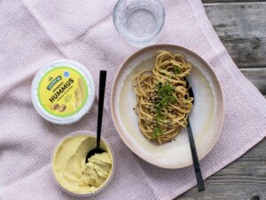 Hummusnuudeliannos kauniilla lautasella Juureva Härkäpapuhummus purkin vieressä